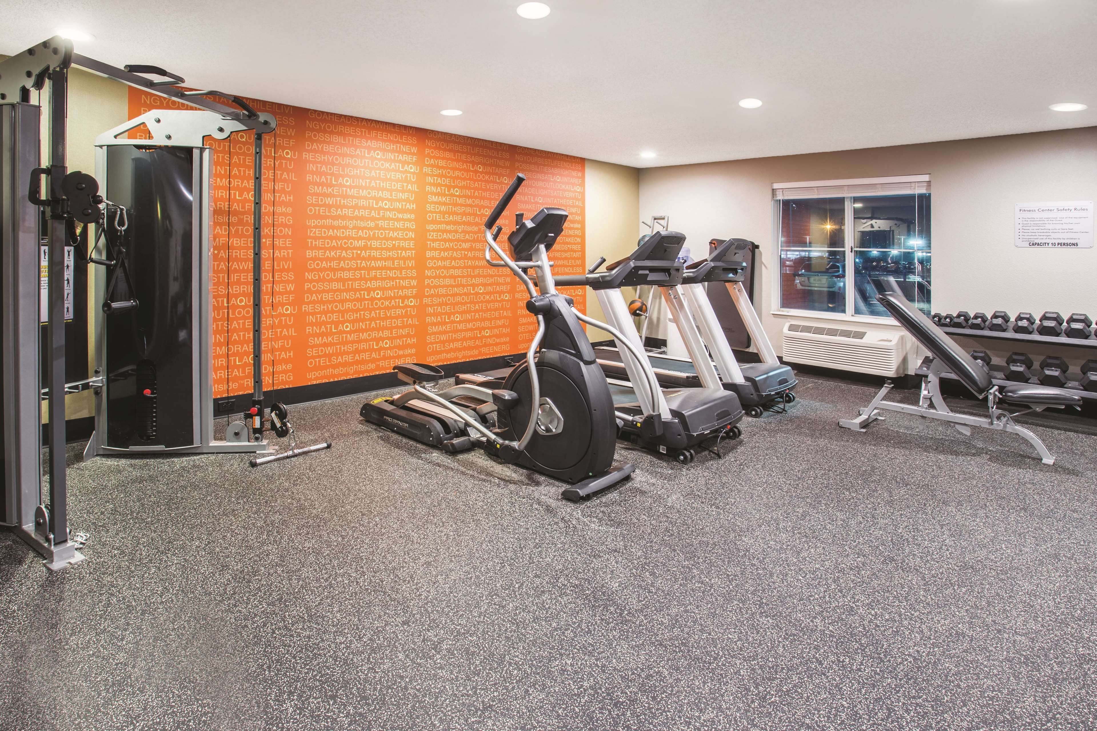 Une salle de sport équipée de machines de cardio, d’haltères et d’un mur orné de messages motivants.