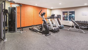 A gym with cardio machines, dumbbells, and a wall with motivational text.