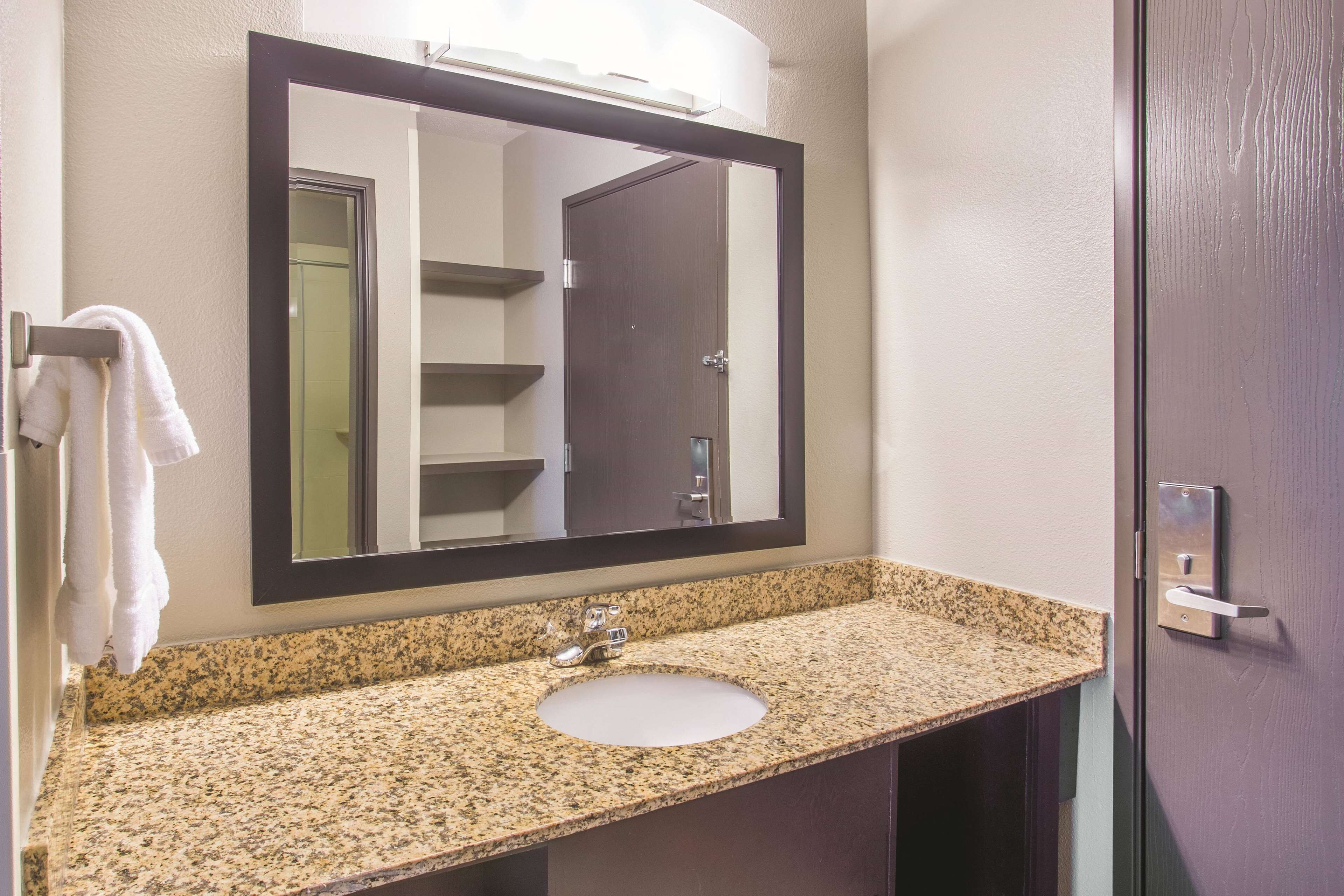 A bathroom with a granite countertop, a sink, a mirror, and a towel rack.