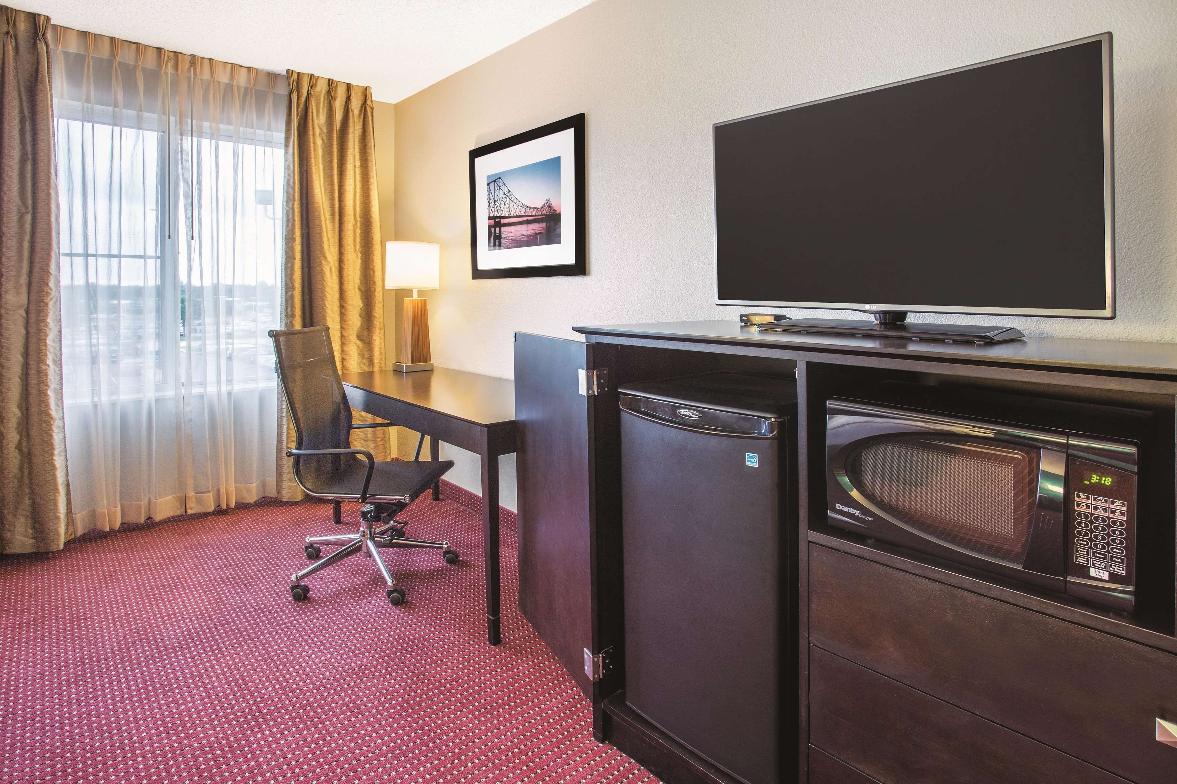 A hotel room with a desk, chair, television, microwave, and a window with curtains.