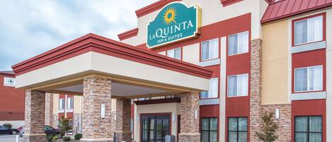 A La Quinta Inn & Suites building with a covered entrance, stone pillars, and a clear sky.