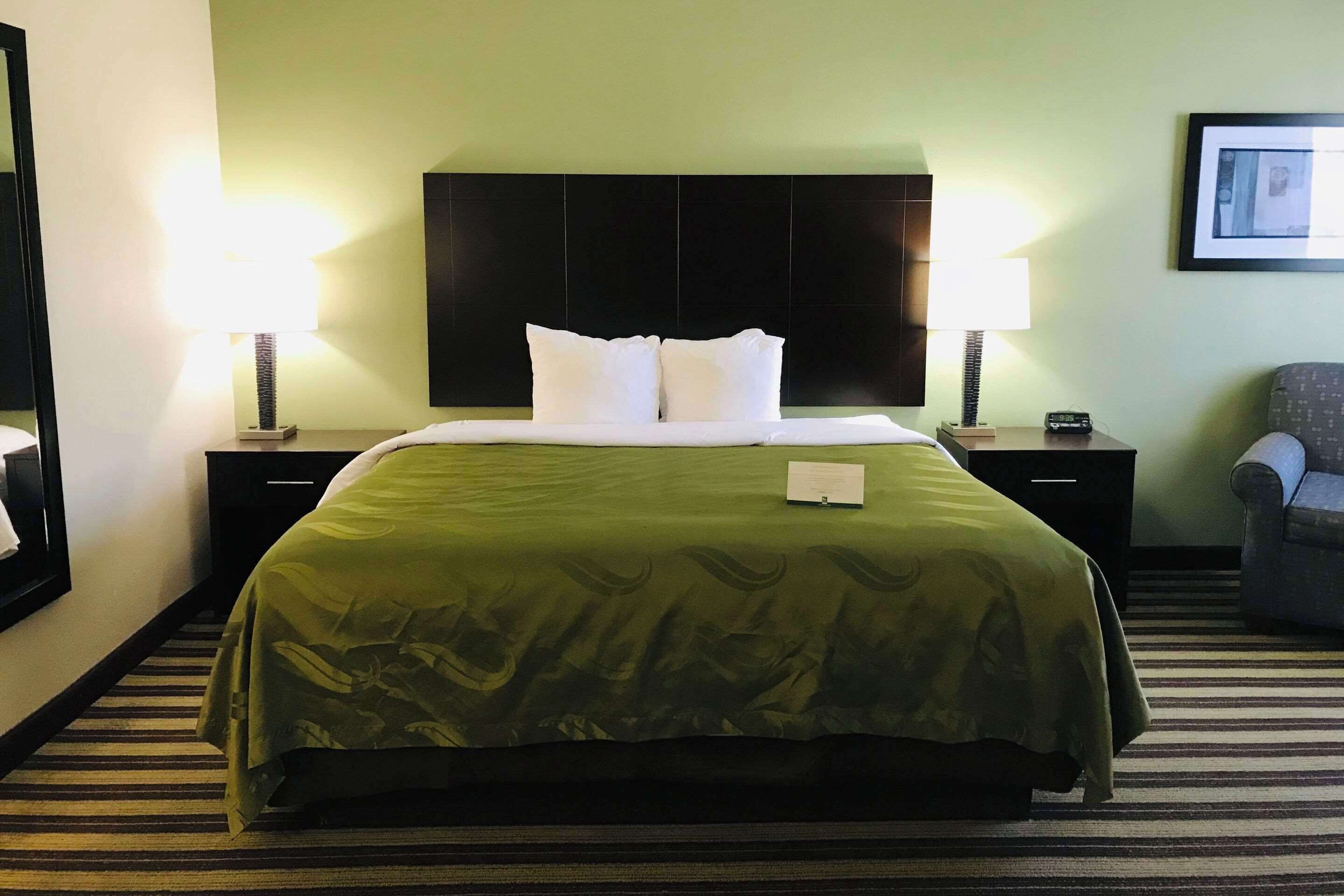 A hotel room with a large bed, two bedside tables, a chair, and a framed picture on the wall.