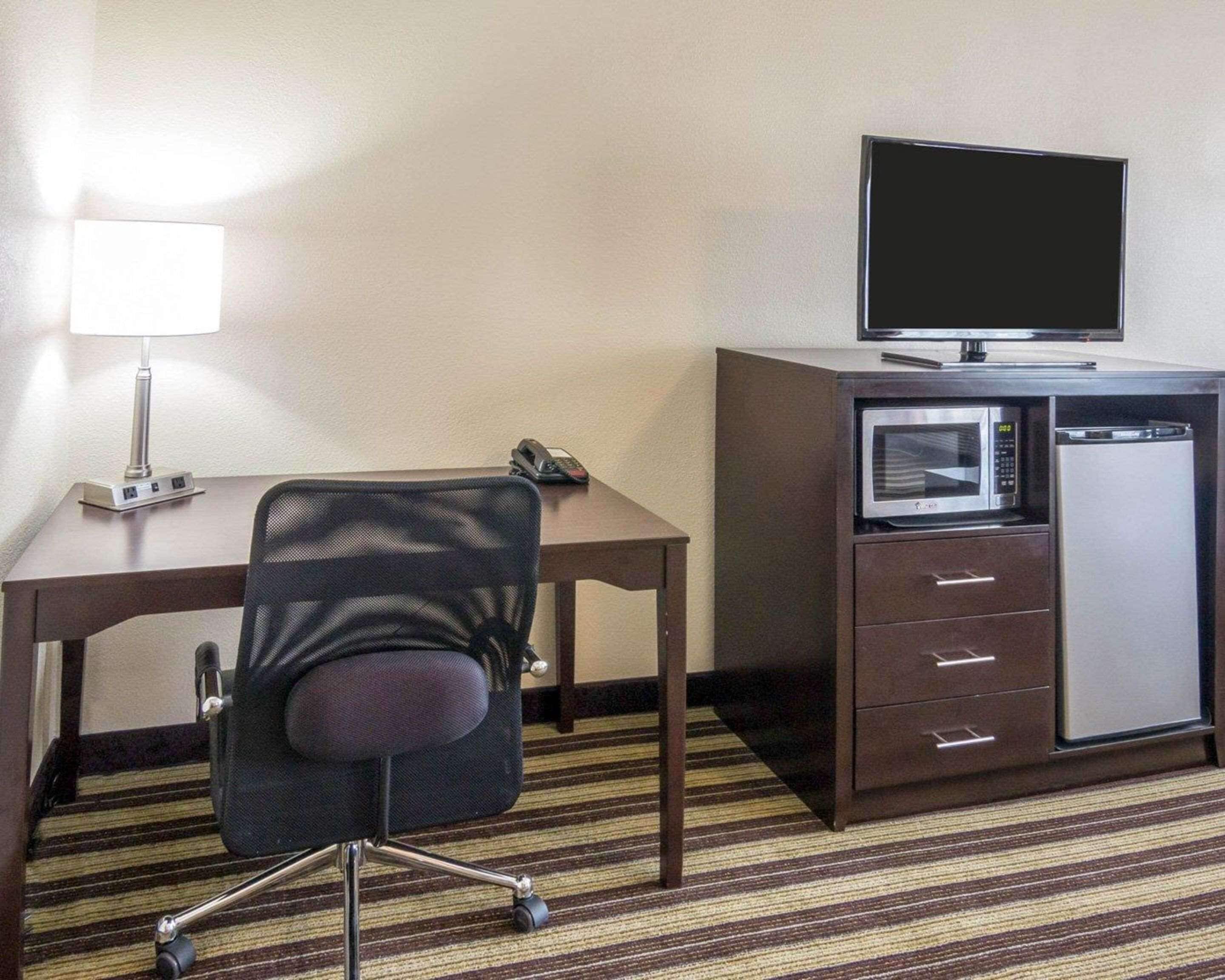 A hotel room with a desk, a chair, a flat-screen TV, a microwave, and a lamp.