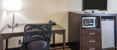 A hotel room with a desk, a chair, a flat-screen TV, a microwave, and a lamp.