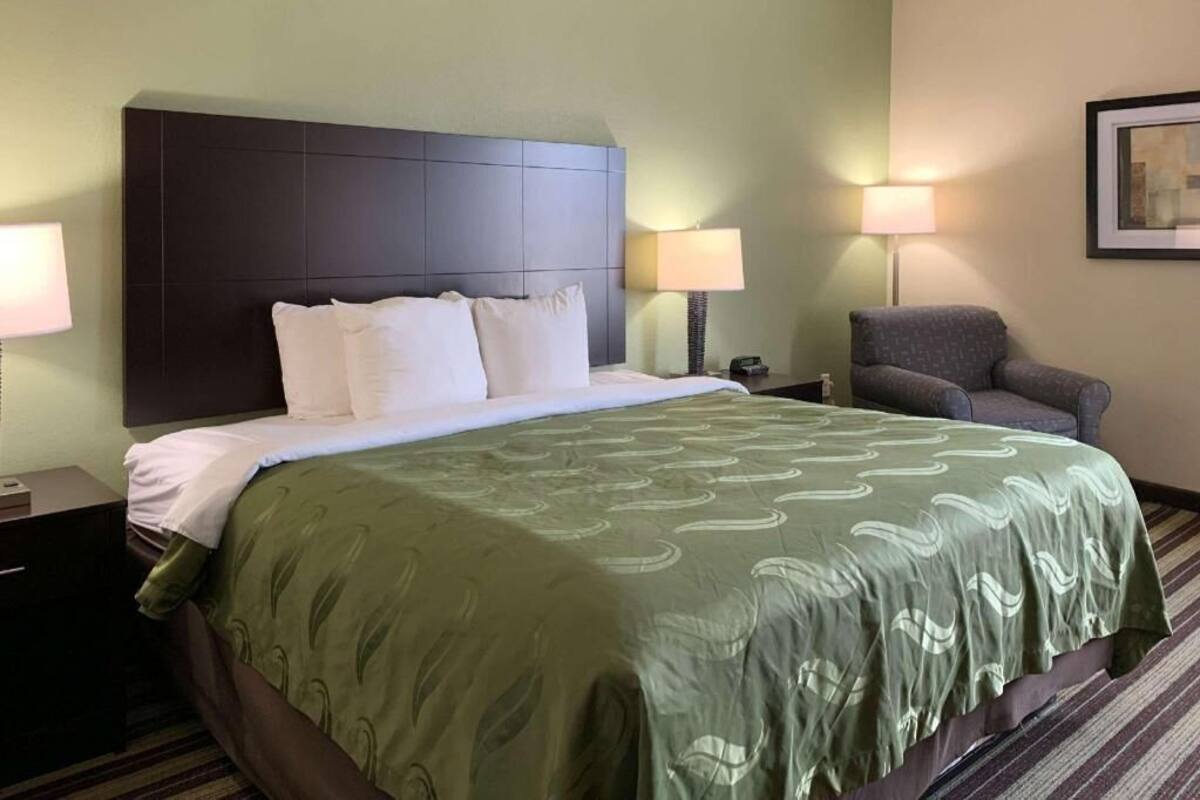 A hotel room with a large bed, a chair, two bedside tables, and a lamp.