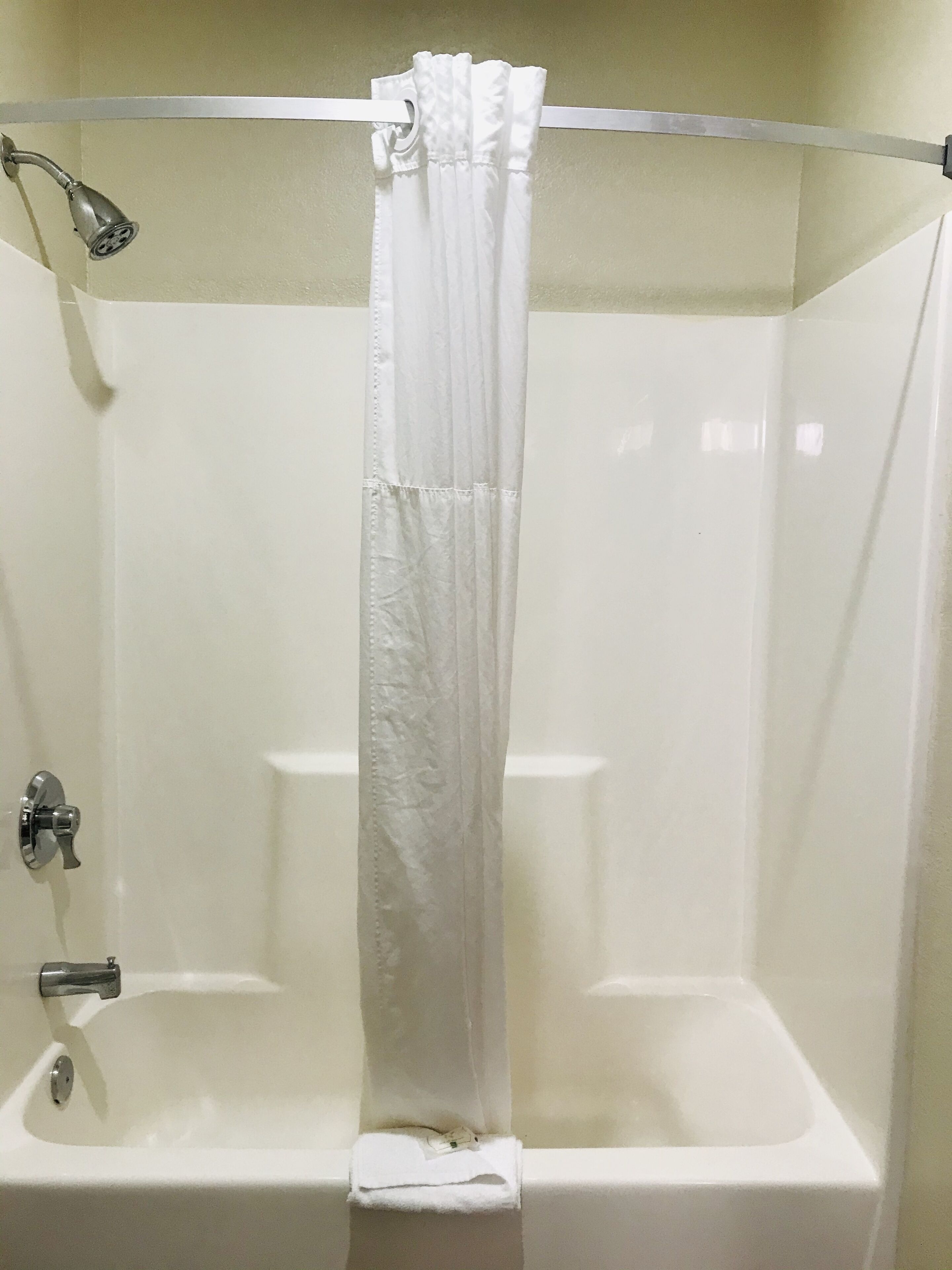A shower area with a white curtain, a handheld showerhead, and a bathtub.