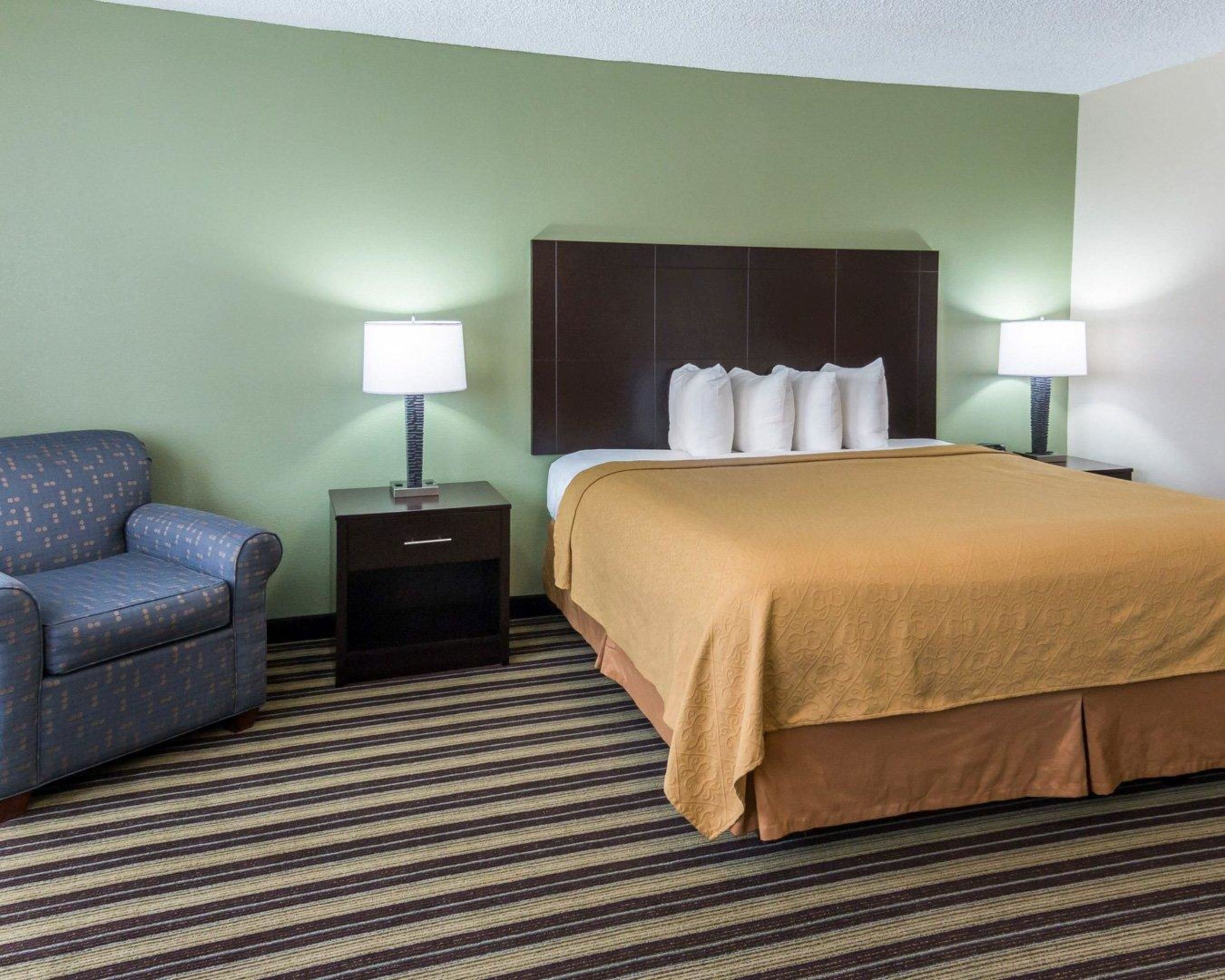 Una habitación de hotel con una cama, dos mesitas de noche, una silla y una alfombra a rayas.