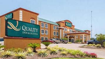 Edificio de Quality Inn & Suites con un cartel, rodeado de jardines ajardinados y vehículos estacionados.