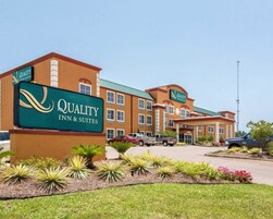 Edificio de Quality Inn & Suites con un cartel, rodeado de jardines ajardinados y vehículos estacionados.