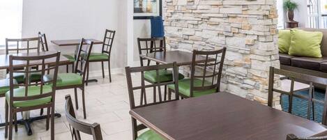 A dining area with tables and chairs, a stone wall, and a sofa with cushions.