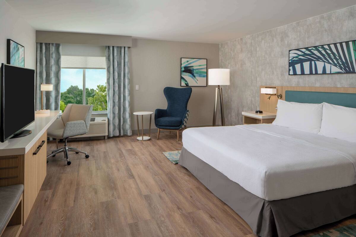 Une chambre d’hôtel comprenant un lit, un bureau avec une télévision, une chaise, une lampe et une vue sur l’extérieur.