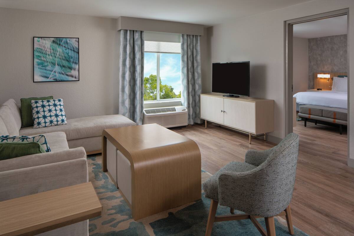 Une chambre d’hôtel avec un canapé, une petite table, un téléviseur posé sur un meuble, un lit et une fenêtre avec des rideaux.