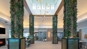 Un vestíbulo espacioso con techos altos, ventanas amplias y una pared vegetal central.