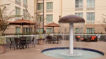 Relax by the central fountain and pool, surrounded by comfortable seating areas with tables and umbrellas.