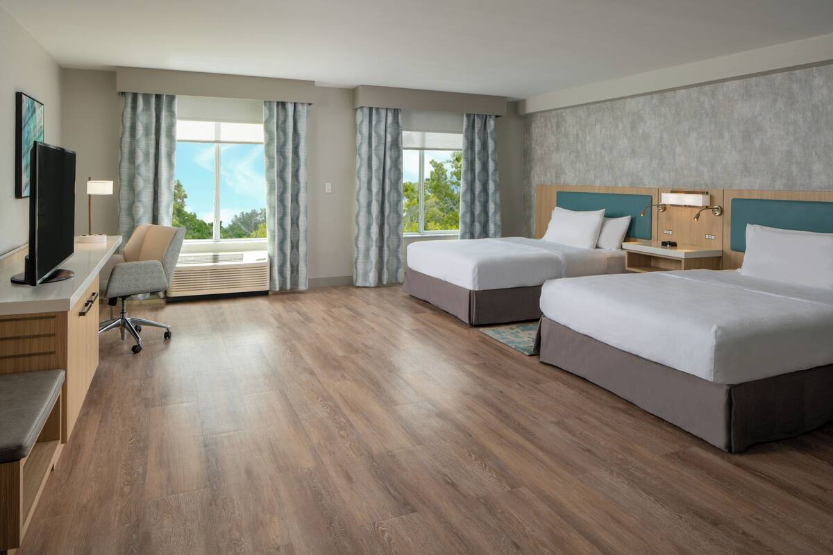 Une chambre d’hôtel avec deux lits, un bureau, une chaise et un téléviseur.