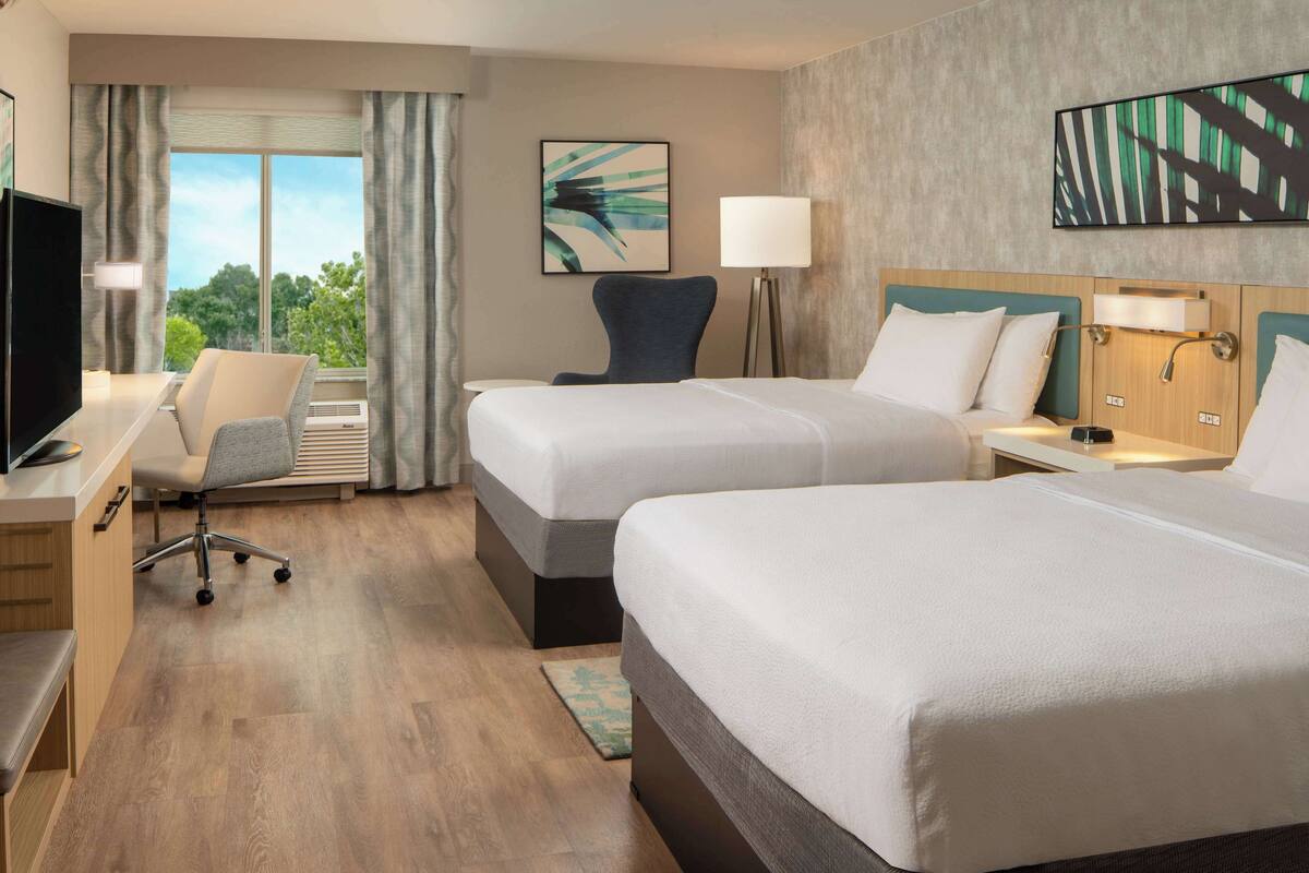 Une chambre d’hôtel avec deux lits, un bureau avec un ordinateur, une chaise et un téléviseur.