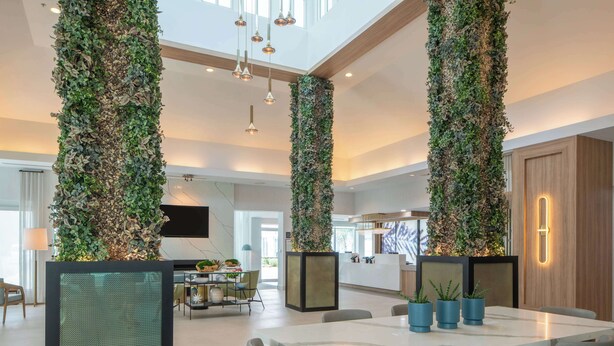 Un moderno vestíbulo de hotel con techos altos, ventanas amplias y jardines verticales en pilares.