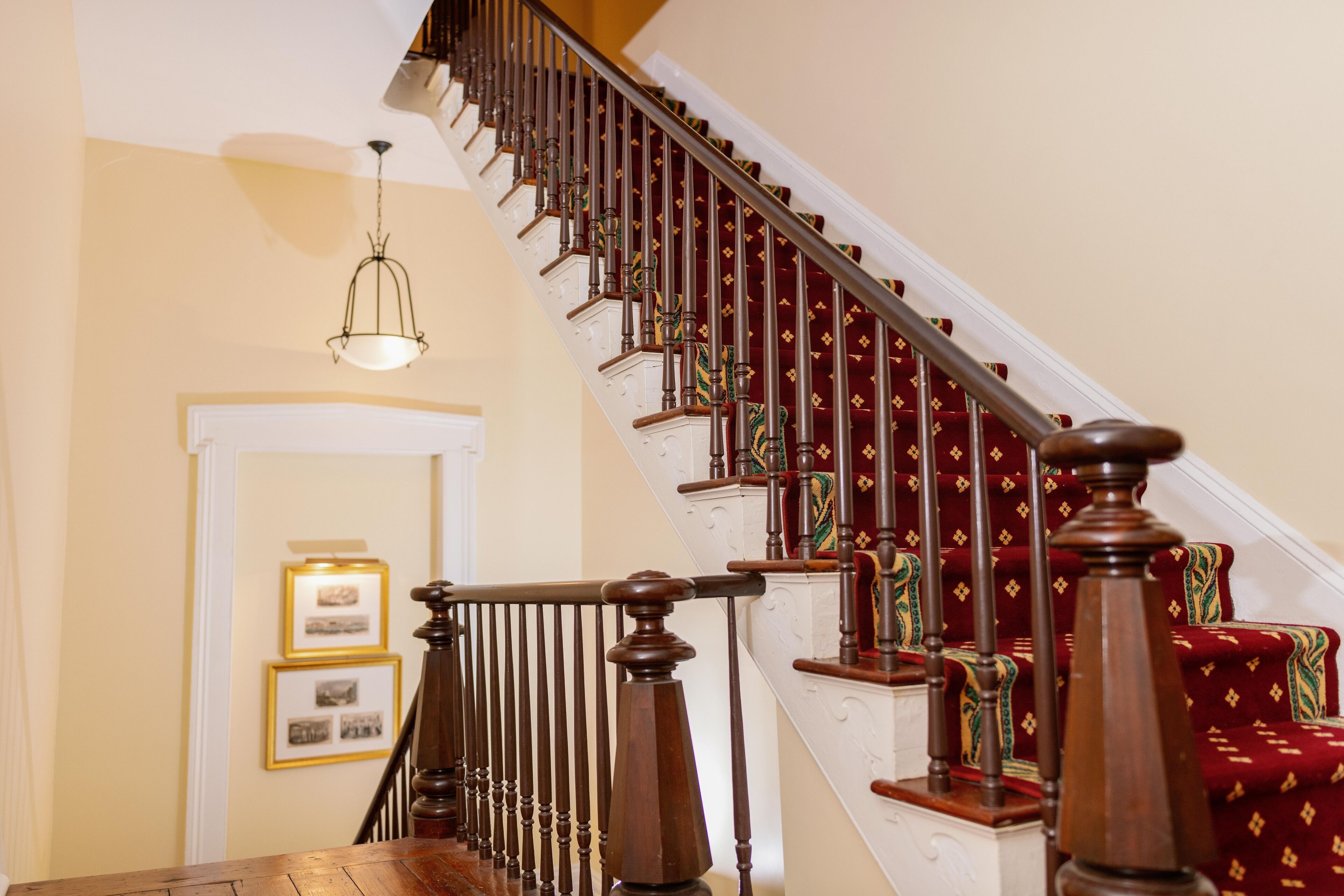 A wooden staircase with a handrail, carpeted steps, and a light fixture above.
