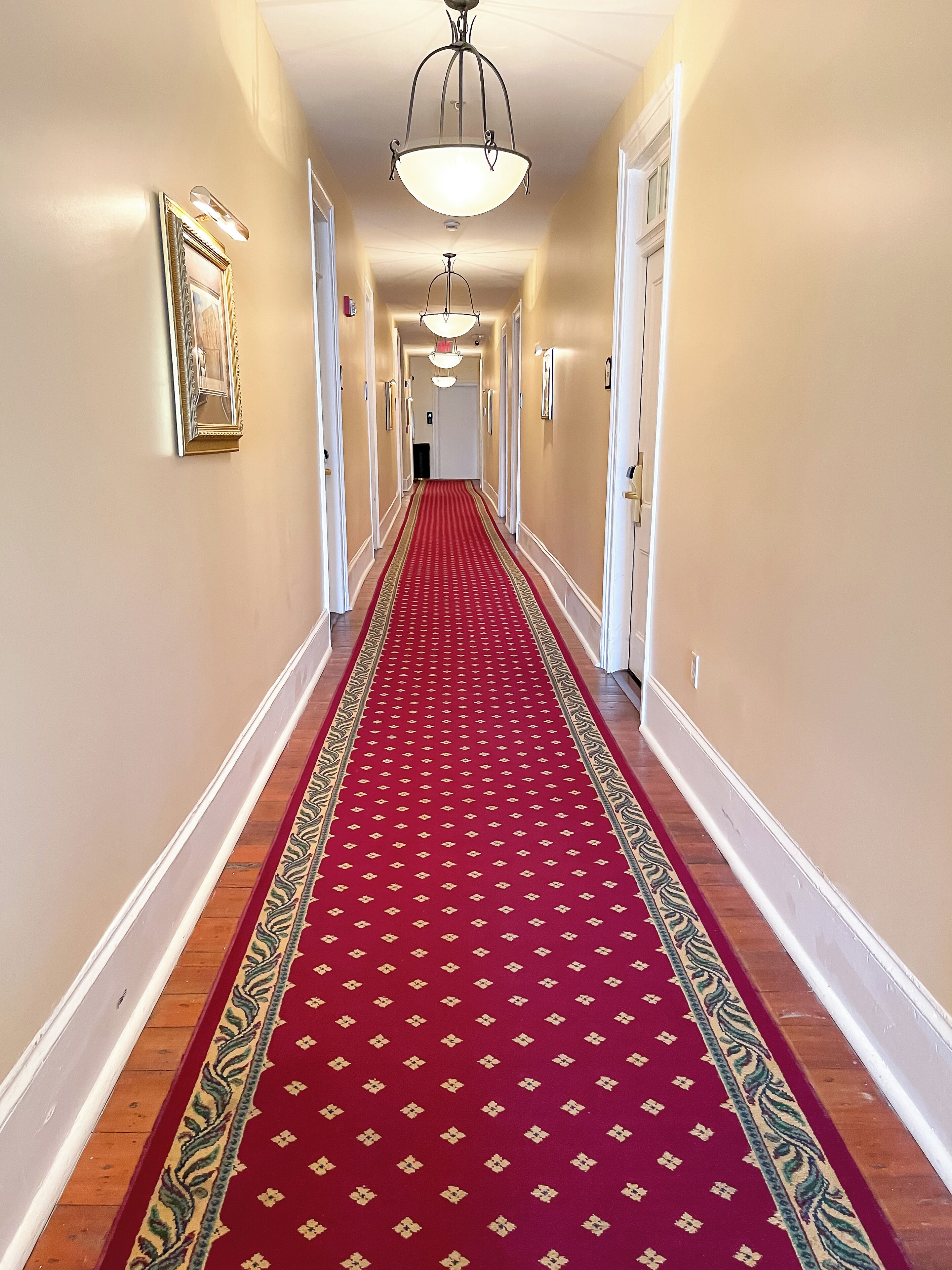 A hallway with a red carpet, white walls, and a chandelier.