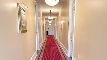 A hallway with a red carpet, white walls, and a chandelier.