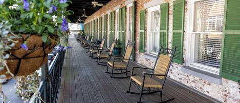 A covered wooden deck with rocking chairs and a hanging flower basket.