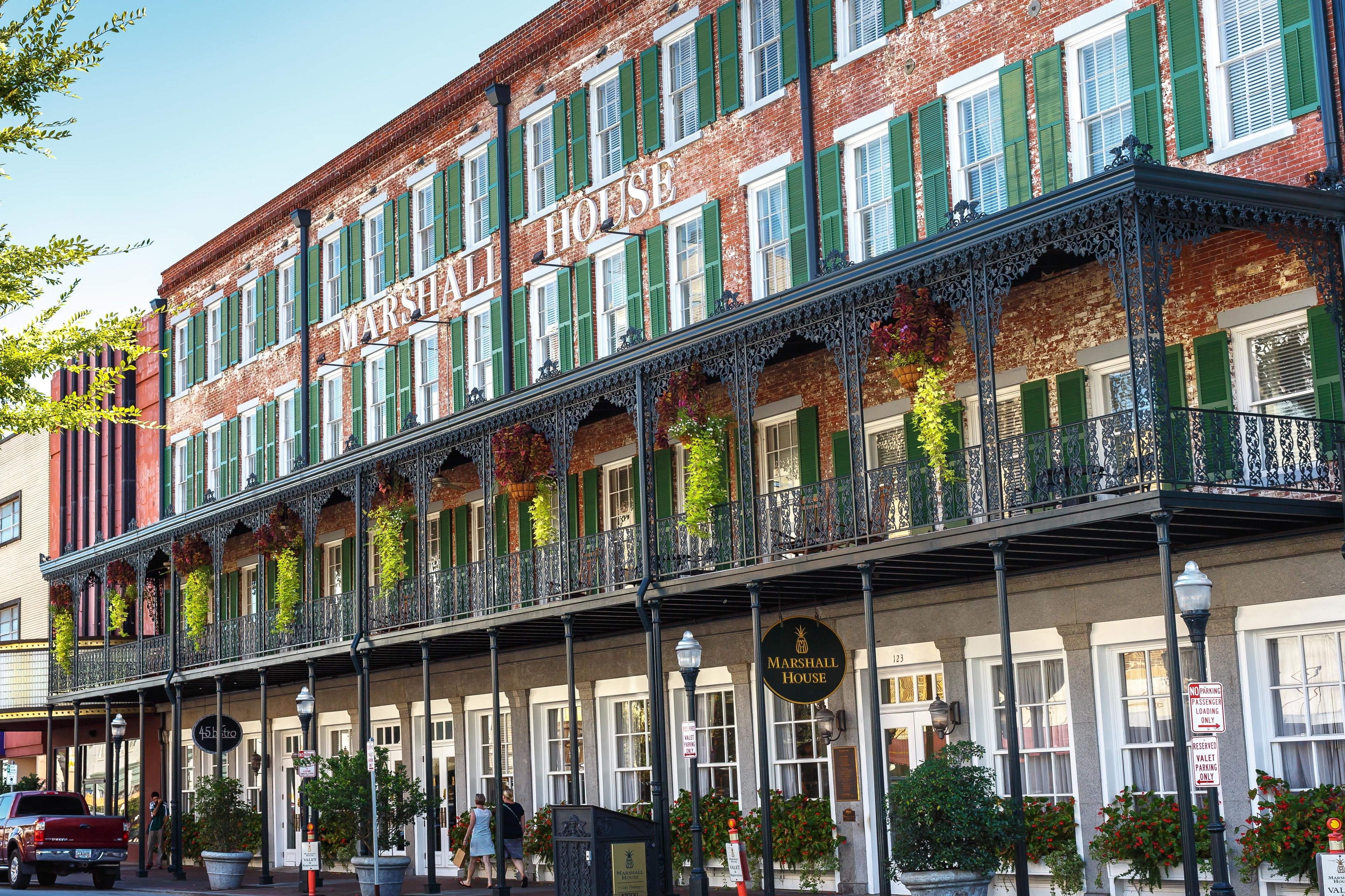 Un edificio histórico con el nombre 'MARSHALL HOUSE' bien visible. Cuenta con un balcón con barandillas de hierro decorativo y macetas con flores colgantes.