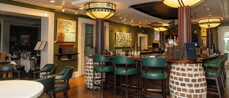 Un interior de restaurante con techos altos, taburetes de bar tapizados en verde y una columna de ladrillo.
