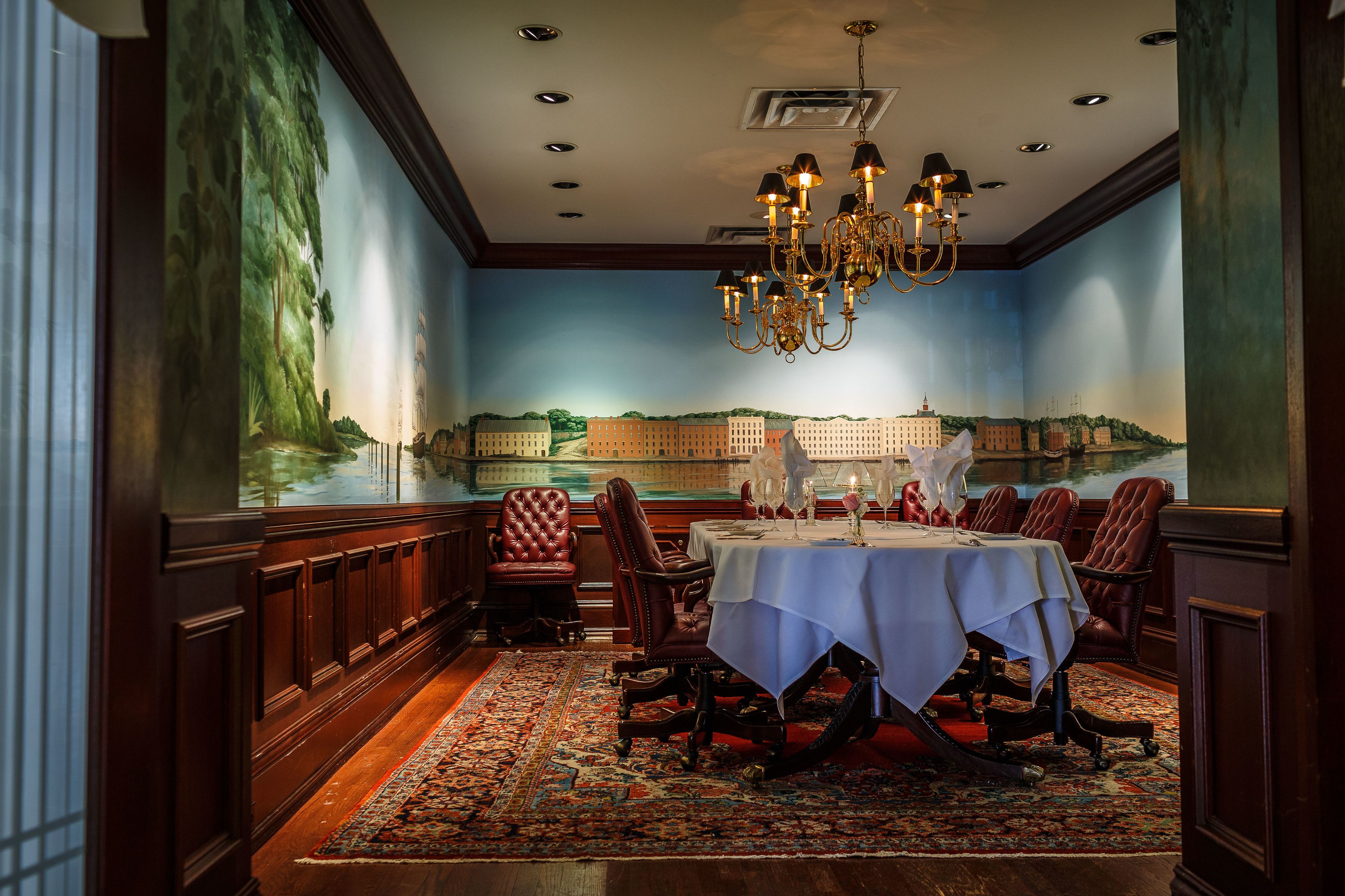 A dining room with a large mural, a chandelier, and a table set for six.