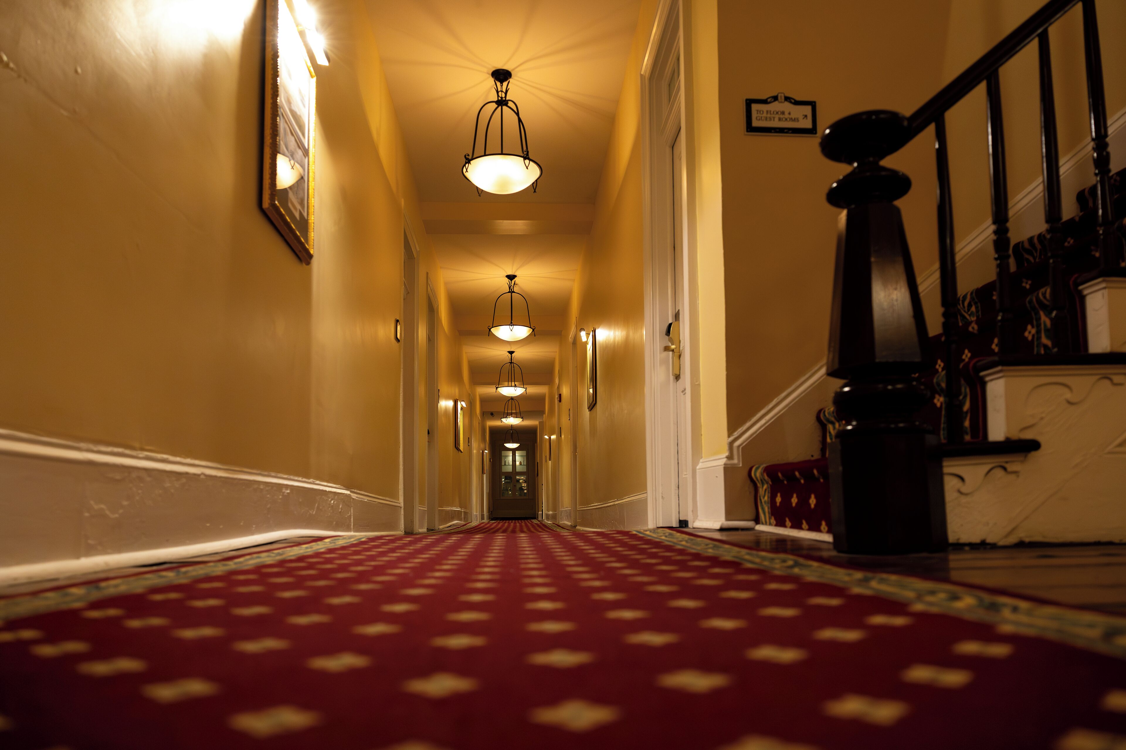 A hallway with a patterned carpet, wall-mounted lights, and a staircase with a handrail.