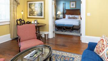 A hotel room with a red armchair, a glass coffee table, a blue sofa, a wooden floor, and a bed with a blue bedspread.
