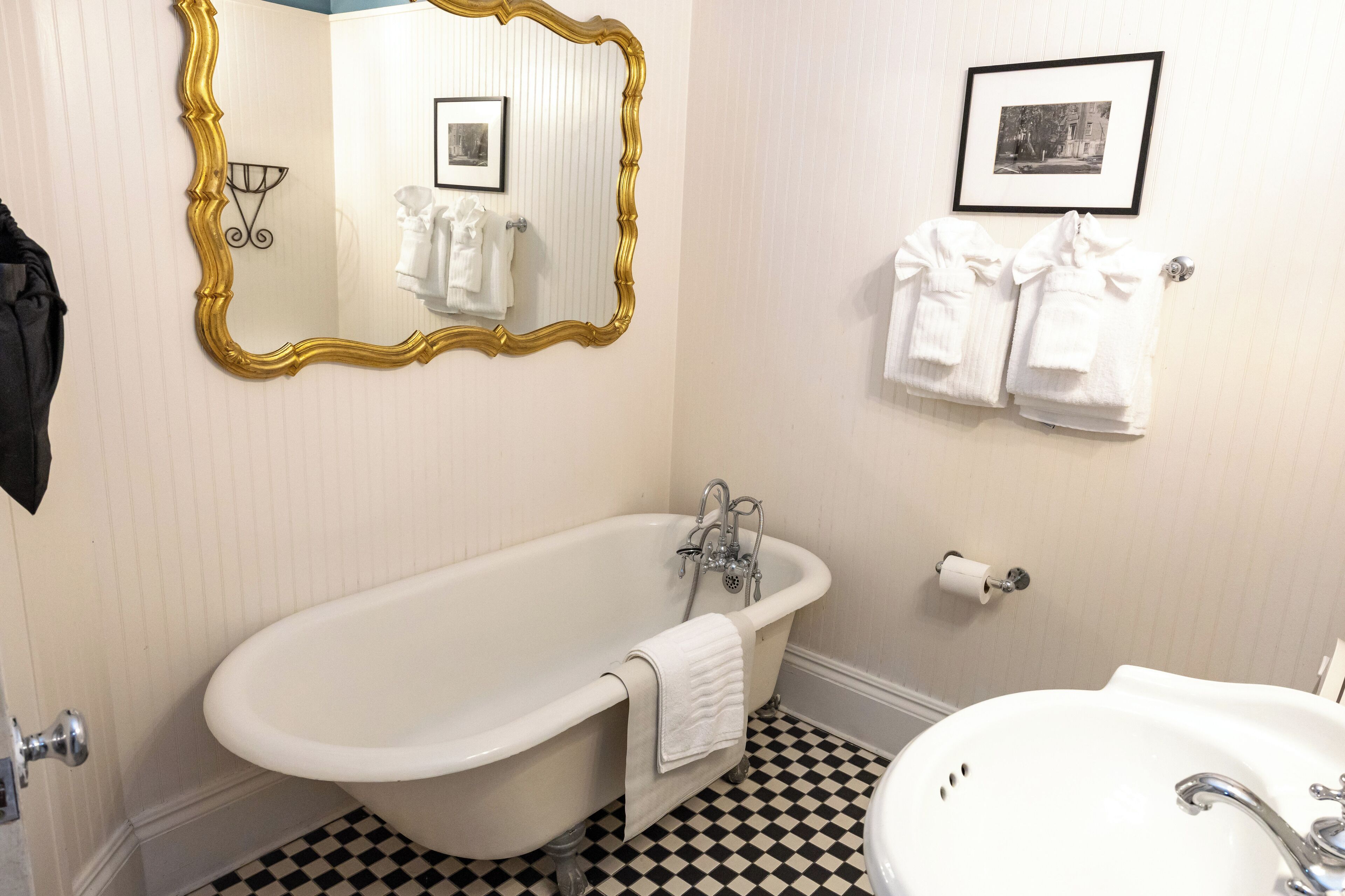 A bathroom with a freestanding bathtub, a sink, a mirror with a gold frame, and towels hanging on a rack.