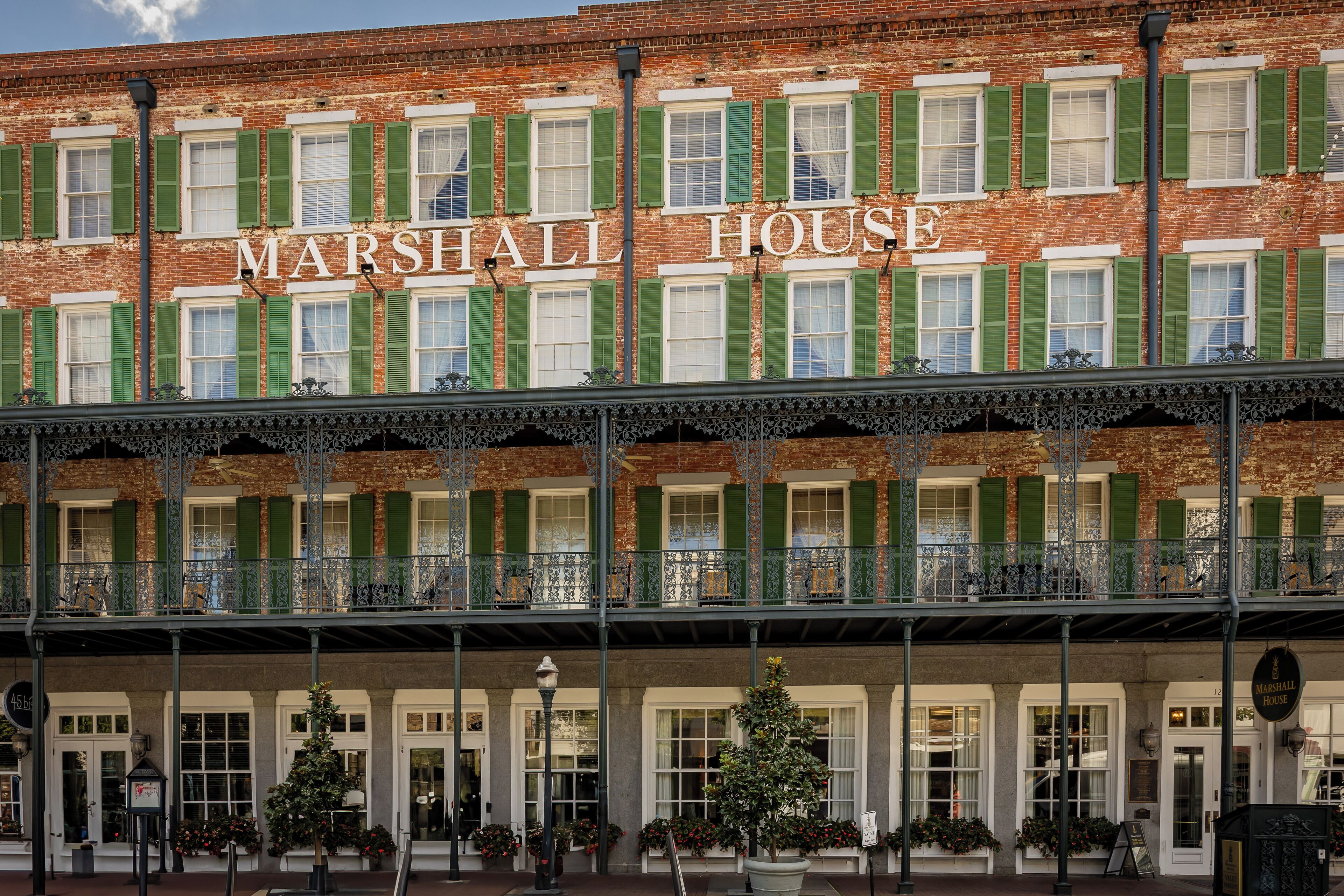 Un edificio histórico llamado 'MARSHALL HOUSE', con fachada clásica, contraventanas verdes y un área de entrada cubierta con plantas en macetas.
