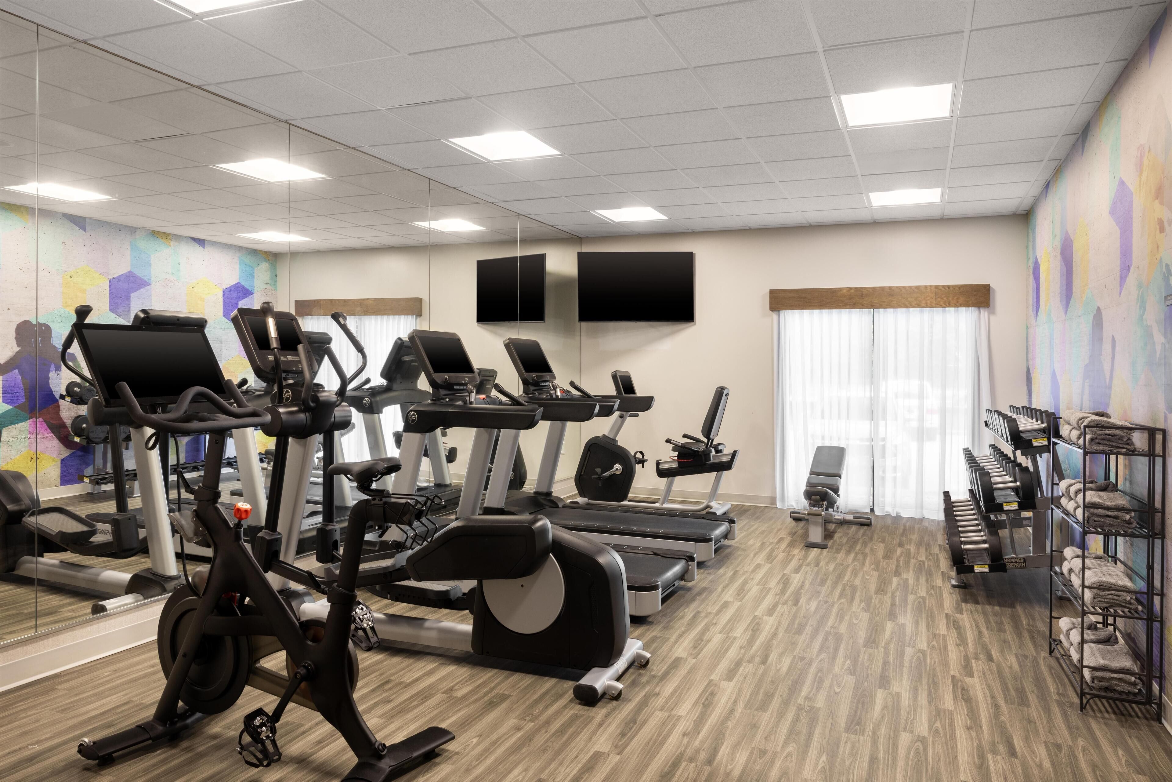 A gym with exercise equipment, mirrors, and a wall-mounted TV.