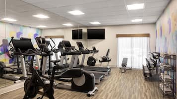 A gym with exercise equipment, mirrors, and a wall-mounted TV.