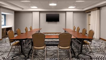 Un salón de conferencias con una mesa larga, sillas, un televisor de pantalla plana y alfombra estampada.