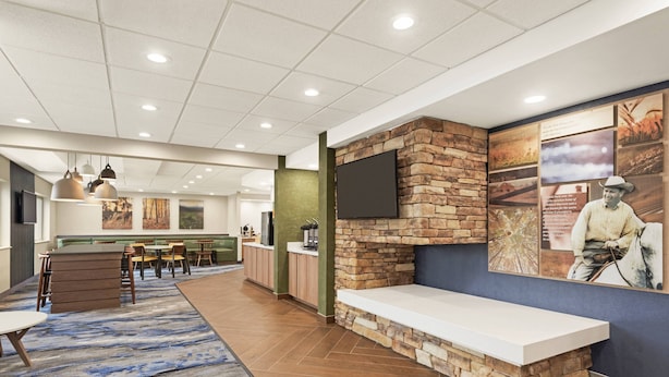 A spacious lobby with a long reception desk, a seating area with tables and chairs, and a large wall-mounted TV.