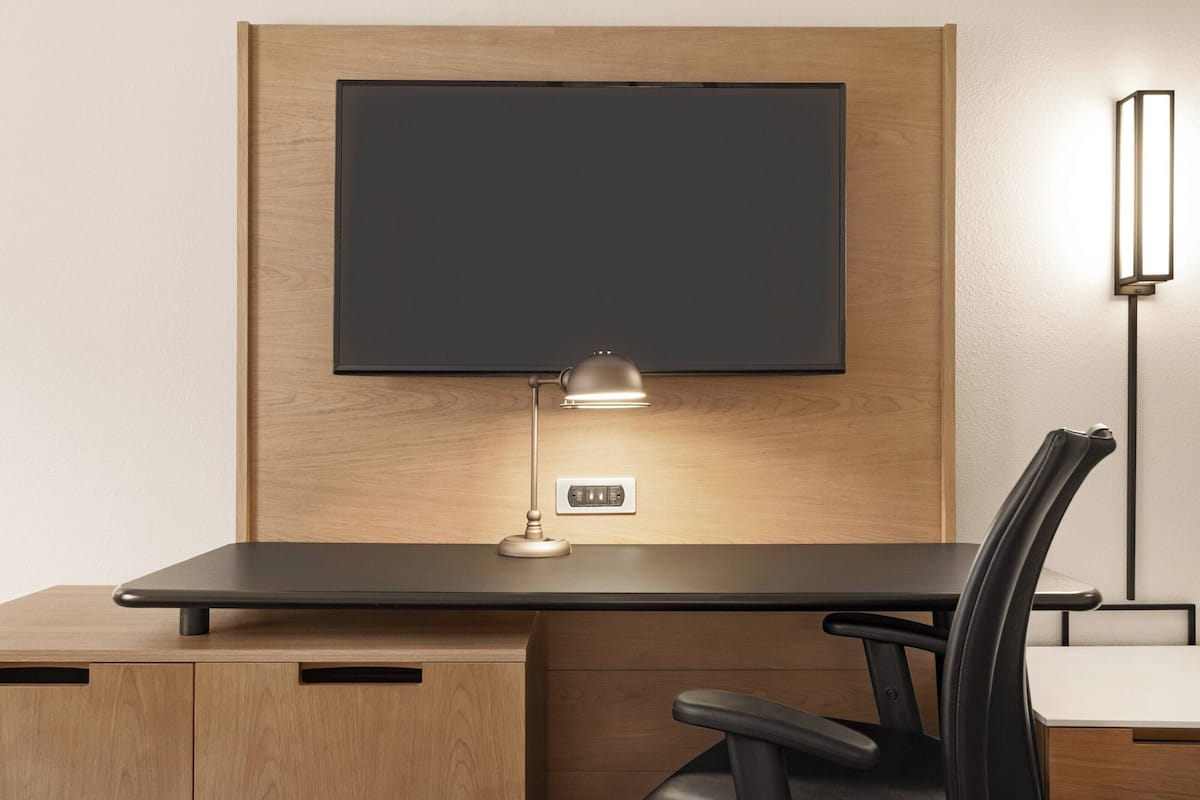 A modern office desk with a mounted flat-screen TV, a desk lamp, and a chair.