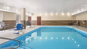 An indoor swimming pool with a tiled deck, a changing room, and a seating area with chairs.