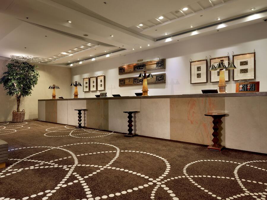 A reception area with a reception desk, framed artwork on the wall, a large potted plant, and a patterned carpet.
