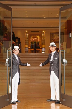 A person in a formal suit and white hat standing at a glass door, with a reflection visible in the glass. - Hotel Royal Hsinchu (Hsinchu)