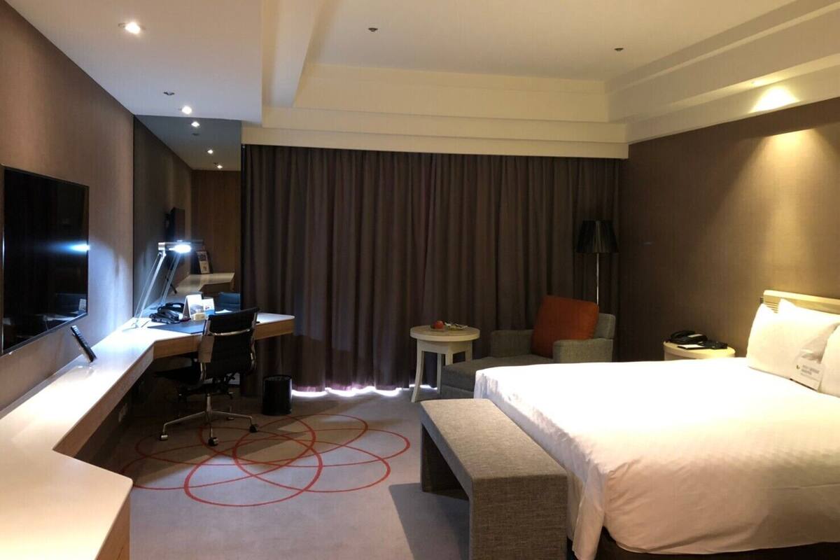 A hotel room with a bed, desk, chair, and a television.