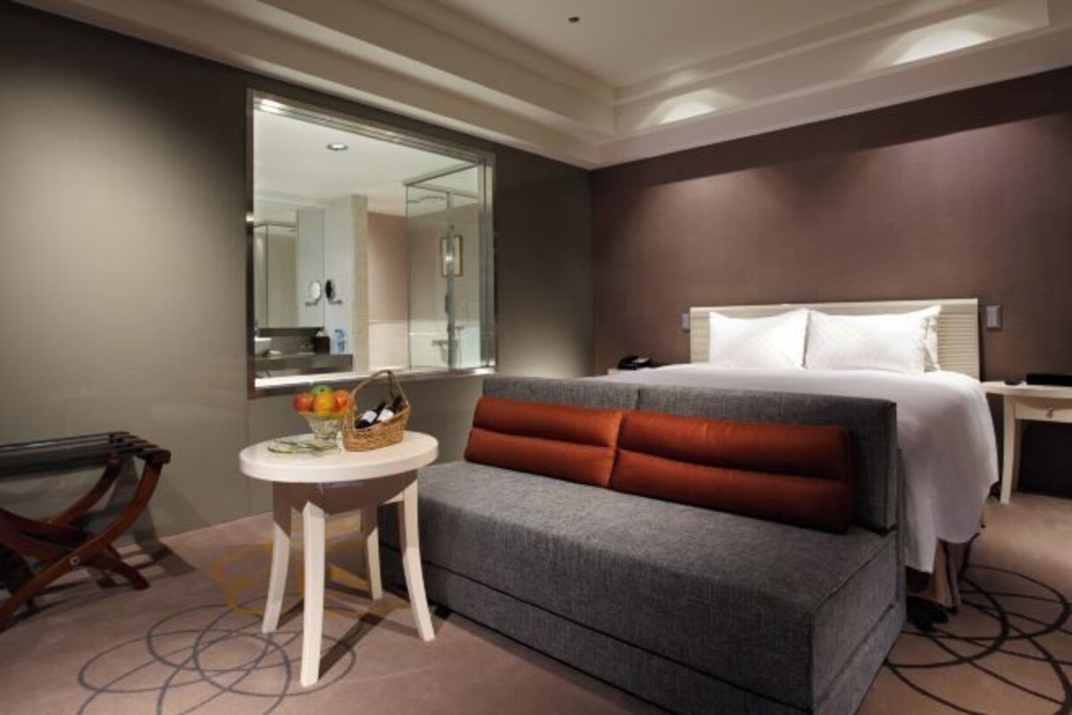 A hotel room with a bed, a small round table with a basket, a mirror, and a view of the bathroom.