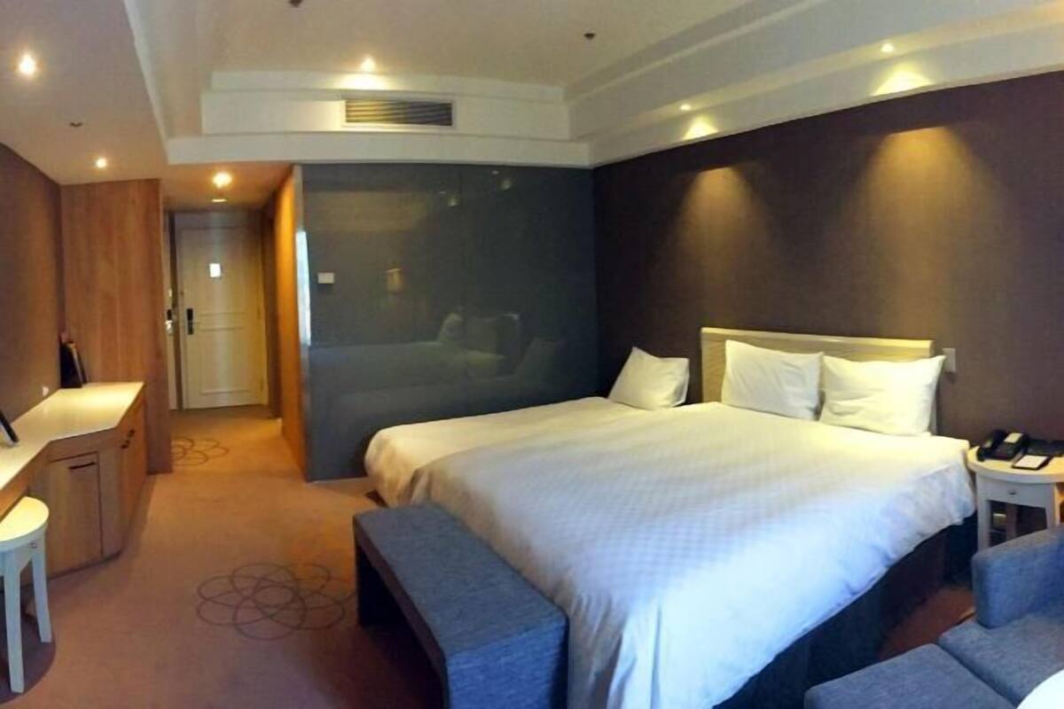 A modern hotel room with a large bed, bedside tables, a desk, and a bench.
