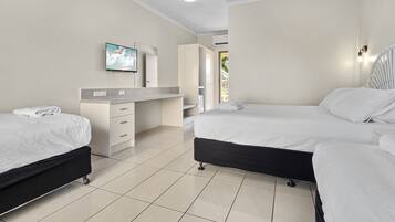 A hotel room with two beds, a desk with a chair, a TV mounted on the wall, and a bathroom visible through an open door.