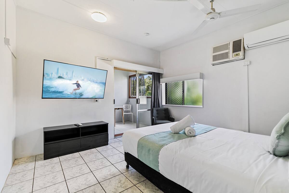 A modern hotel room with a bed, a TV mounted on the wall, a desk, and a chair.
