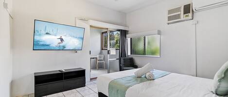 Una habitación de hotel moderna con una cama, un televisor montado en la pared, un escritorio y una silla.