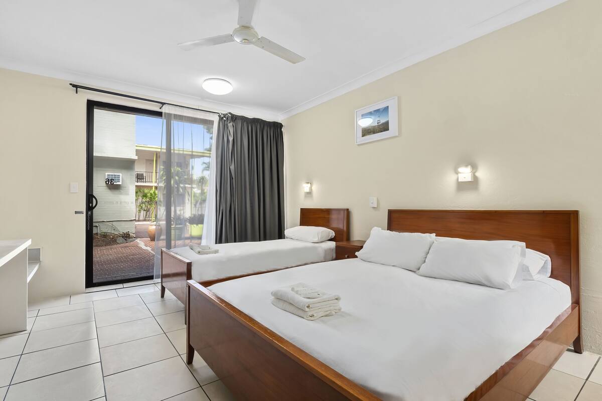 A hotel room with a large bed, a smaller bed, a bathroom, and a sliding glass door leading to an outdoor area.