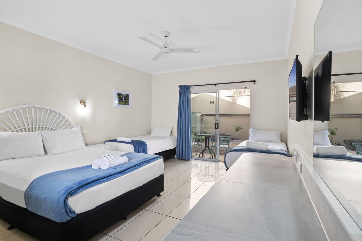 A hotel room with a bed, a desk, a chair, a ceiling fan, and a sliding glass door to an outdoor area.