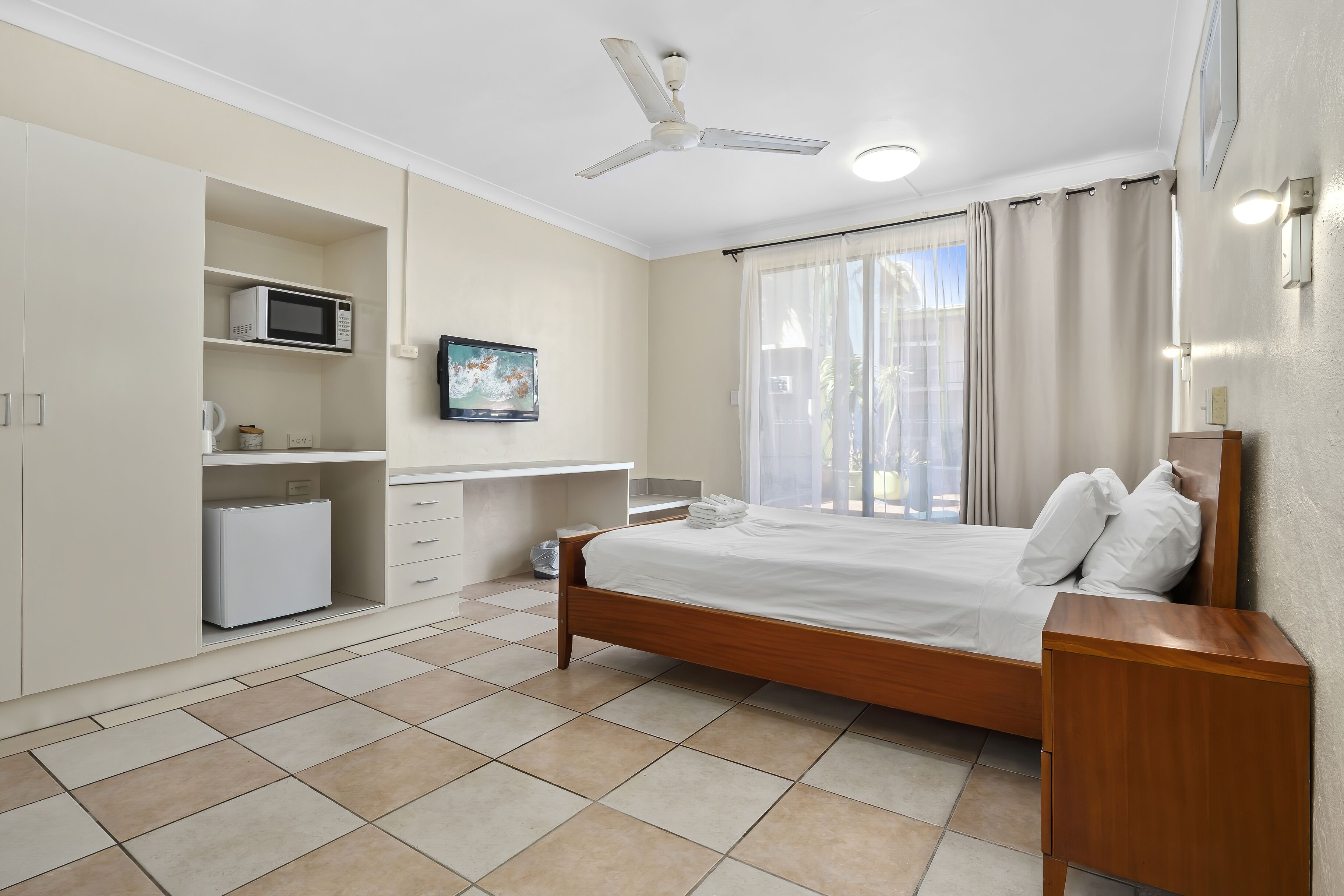 A hotel room with a bed, a desk, a microwave, a TV, and a ceiling fan.