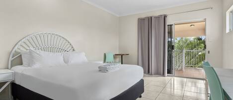 A hotel room with a bed, a desk, a chair, a ceiling fan, and a view of the outside.